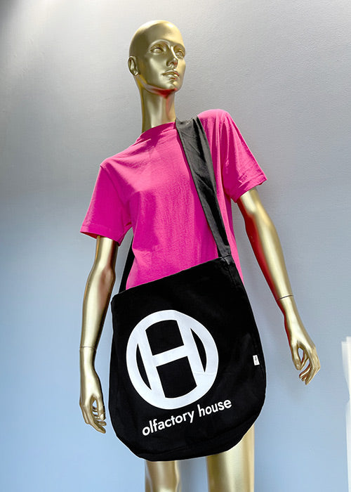 A black canvas tote bag with a white Olfactory House logo on the front. The strap is long enough to wear crossbody and  is approximately 3 inches wide. 